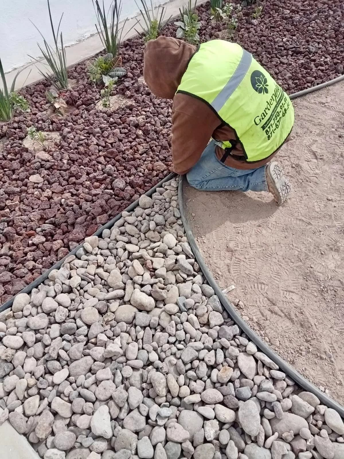 Trabajador de Garden Plus acomodando piedra de río junto a piedra roja y separador negro