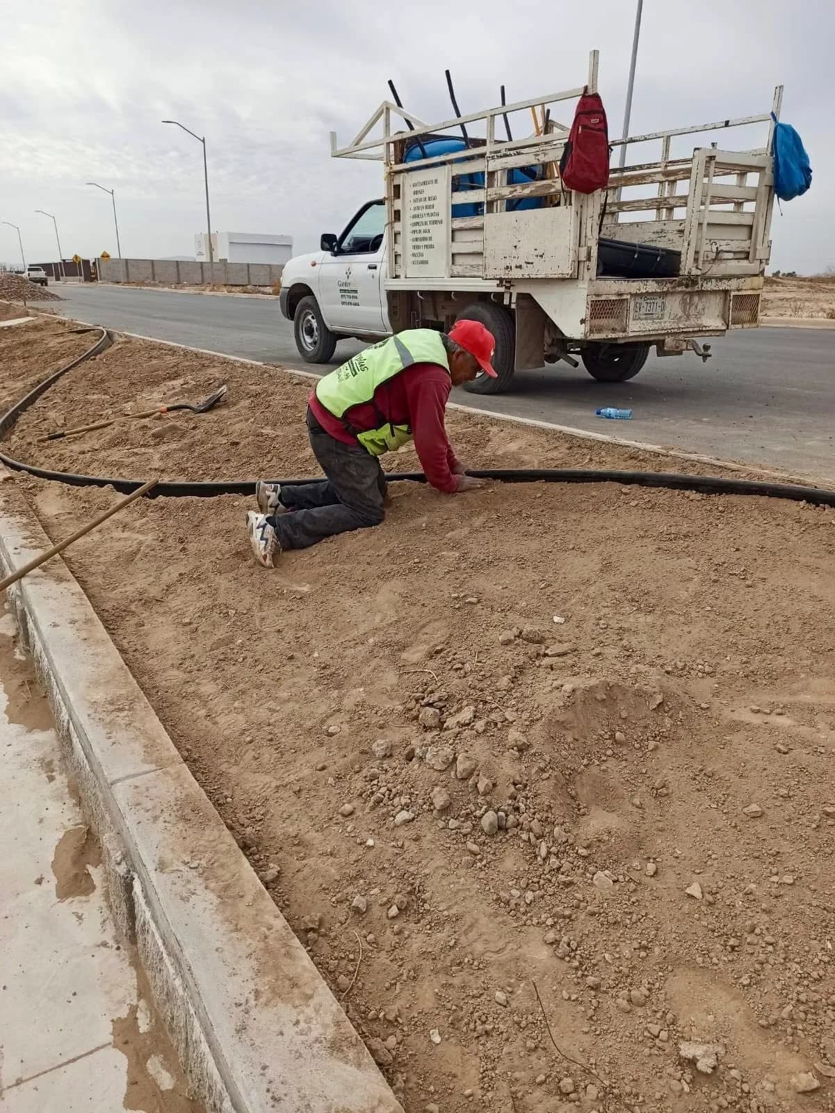Trabajador de Garden Plus tendiendo manguera de riego en un camellón, con la camioneta de la empresa al fondo